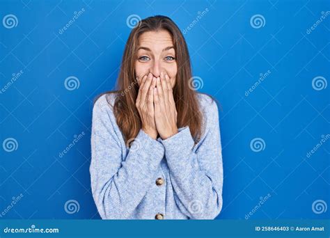 Young Woman Standing Over Blue Background Laughing And Embarrassed Giggle Covering Mouth With