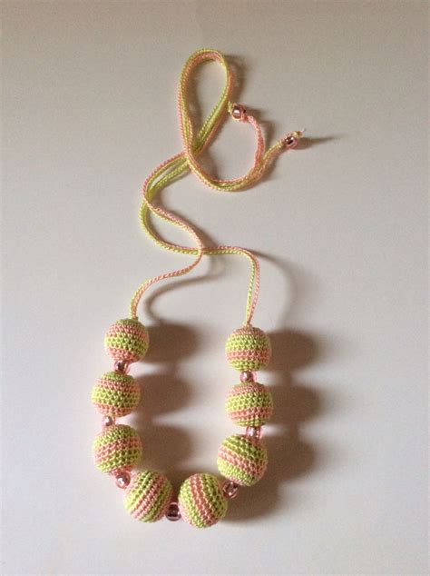 A Beaded Necklace On A White Surface With A Pink And Yellow Ribbon