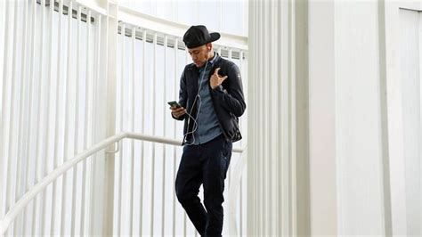 A Man Standing On The Stairs Looking At His Cell Phone And Listening To