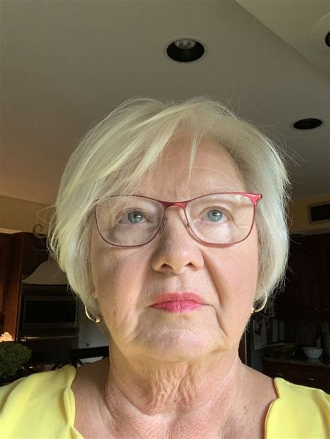 An Older Woman With Glasses And Yellow Shirt Looking At The Camera While Standing In A Kitchen