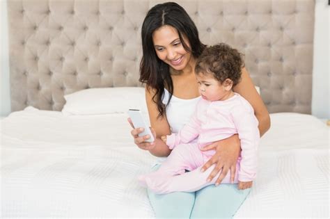 Premium Photo Smiling Brunette Holding Her Baby And Using Smartphone