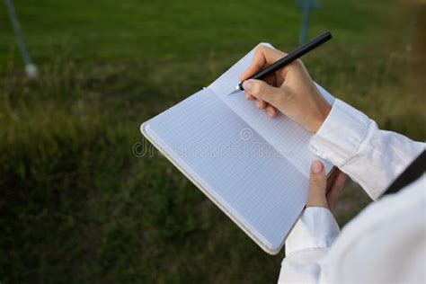 The Girl Makes Notes In A Notebook With A Black Pen In Nature View