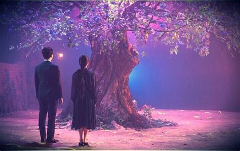 two people standing in front of a tree with purple lights on the trunk ...