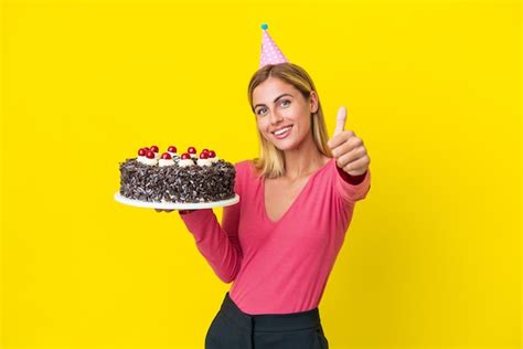Fille Blonde Uruguayenne Tenant Un Gâteau D anniversaire Isolé Sur Fond Jaune Avec Les Pouces