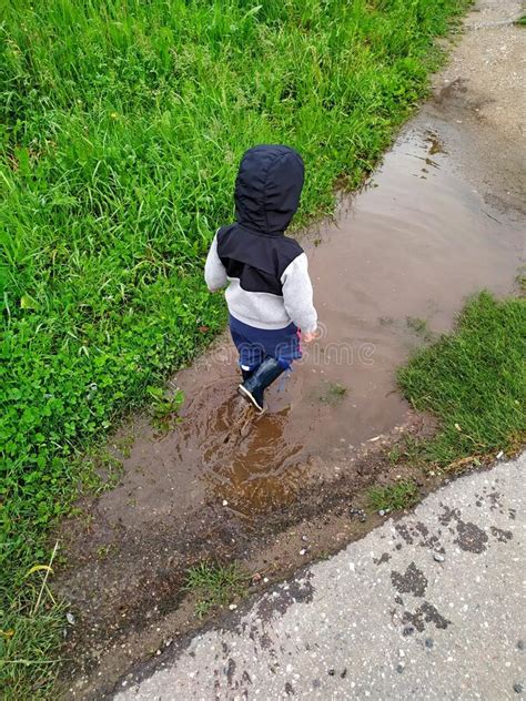 Little Boy Walks Through A Puddle In Rubber Boots Carefree Summer