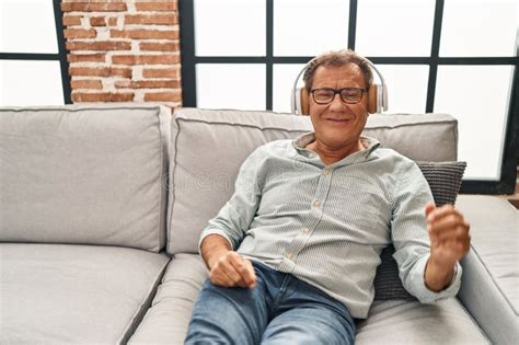 Middle Age Man Listening To Music Sitting On Sofa At Home Stock Image