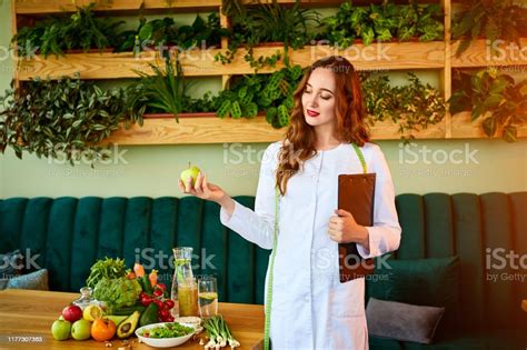 Woman Dietitian In Medical Uniform With Tape Measure Holds Apple