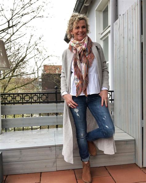 A Woman Is Standing On The Porch Wearing Jeans And A Cardigan Sweater