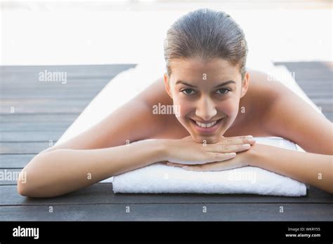 Happy Brunette Lying On A Towel Poolside Outside At The Spa Stock Photo