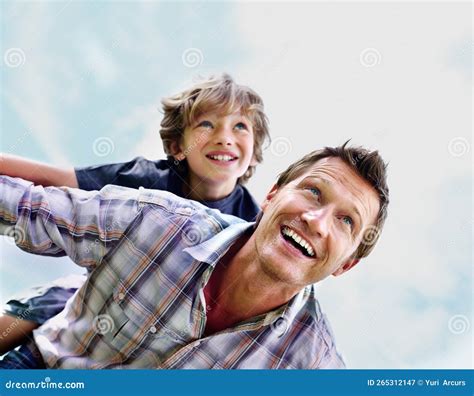 Cheerful Mature Man With His Son On Back Flying Against Sky Portrait