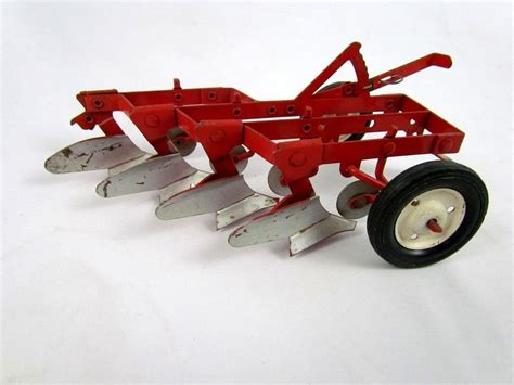 A Red Toy Tractor With Four Plow Blades