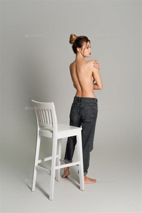 Back View Of Half Naked Woman In Jeans Standing Near White Chair And