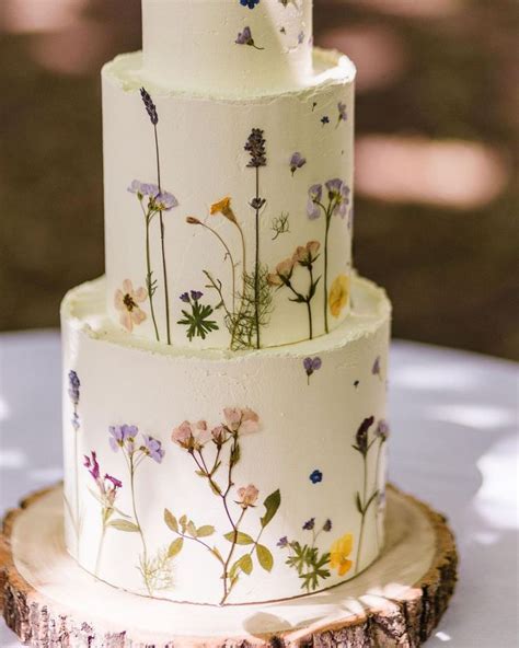 A Three Tiered Wedding Cake Decorated With Wildflowers On A Tree Stump