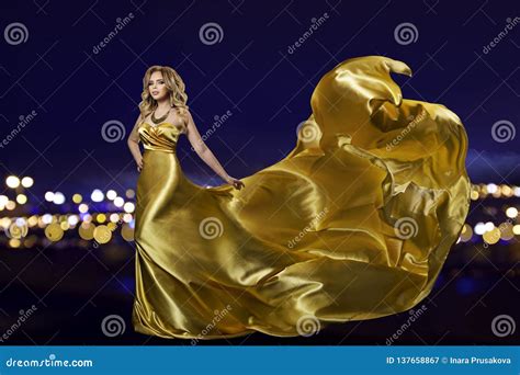 Woman In Gold Dress Over Night City Fashion Model In Long Golden Gown