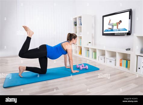 Young Pregnant Woman Exercising On Exercise Mat By Watching Television