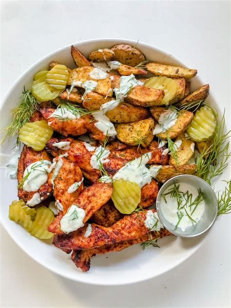 A White Plate Topped With Chicken And Potatoes Covered In Ranch