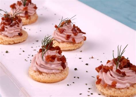 Small Crackers Topped With Bacon And Garnish Sit On A White Platter