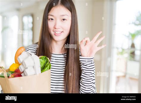 Beautiful Asian Woman Holding Paper Bag Of Fresh Groceries Doing Ok