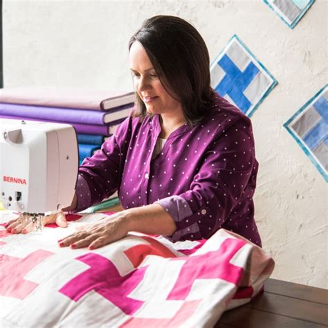 A Woman Sitting At A Table With A Sewing Machine On It S Side And Quilting Behind Her