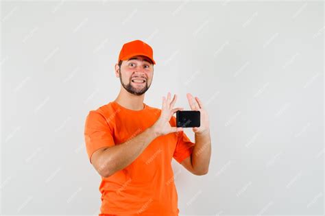 Free Photo Delivery Man In Orange T Shirt Cap Taking Photo On Mobile