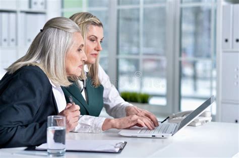 Two Mature Businesswomen Sitting At Table With Laptop And Working Stock