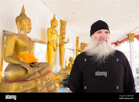 Happy Mature Bearded Tourist Man Thinking Beside Golden Buddha Statue
