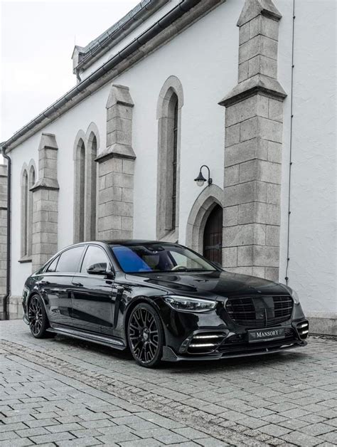 A Black Car Is Parked In Front Of A White Building On A Cobblestone Street