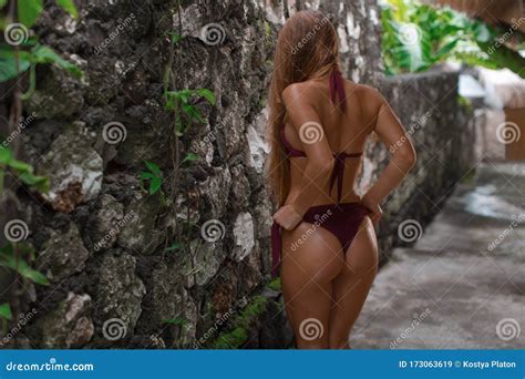 Tanned Brunette In Bikini Posing With Her Back Near Stone Wall In Tropics Stock Image Image Of