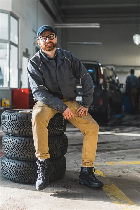 Full Vertical Shot Of An Auto Mechanic Sitting On Wheels And Smiling