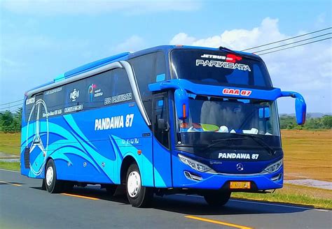 A Blue Bus Driving Down The Road Next To A Grass Covered Field With