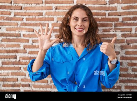 Beautiful Brunette Woman Standing Over Bricks Wall Showing And Pointing Up With Fingers Number