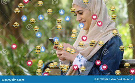 Animation Of Od Falling Emojis Over Woman In Hijab Using Smartphone