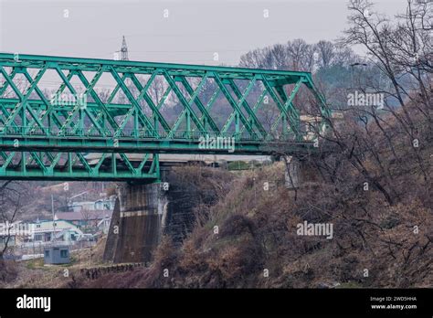 Two Green Railroad Bridges On The Bank Of A River With Houses In The