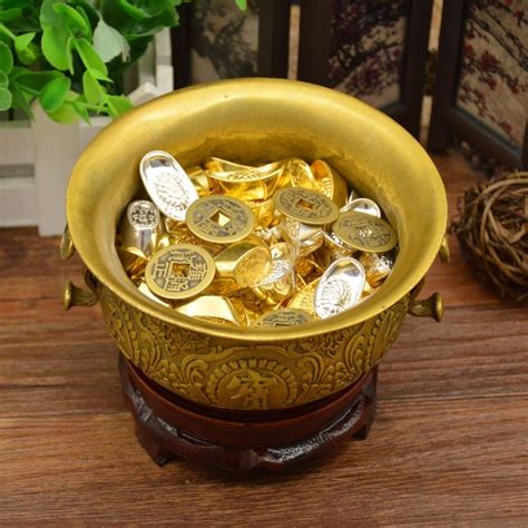 gold coins are in a bowl on a wooden table next to a potted plant