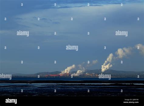 Industrial Landscape With Smokestacks Emitting Smoke Over A Coastal