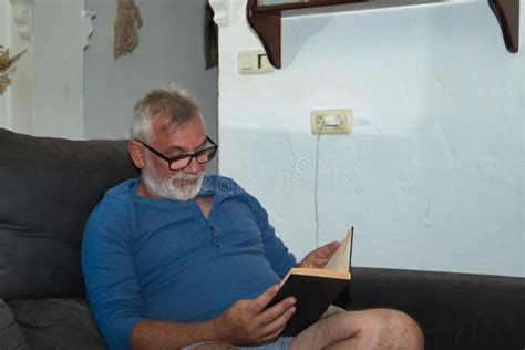 Mature Gray Haired Man With Beard And Glasses In Pajamas Sitting On