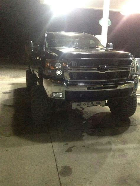 A Large Black Truck Parked In Front Of A Gas Station With Its Lights