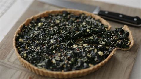 A Tart Crust With Spinach And Other Toppings Next To A Knife On A Cutting Board