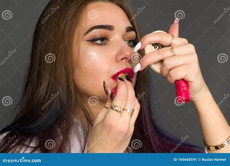 Brunette Girl Paints Her Lips With Lipstick Looking In A Small Mirror On A Dark Background