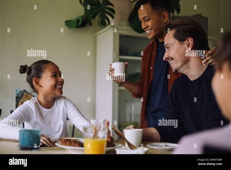 Happy Gay Couple With Daughter Having Breakfast While Sitting At Dining Table In Home Stock