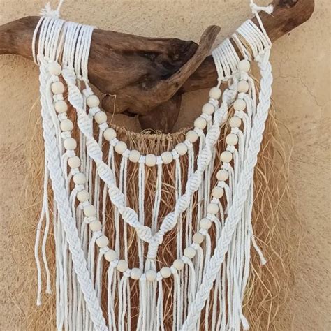 A Piece Of Driftwood Is Adorned With White Macrame Beads And Tassels