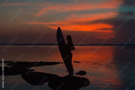 Silhouette Surfer Woman In Bikini On Tropical Beach Holding Surfboard At Sunset Stock Photo