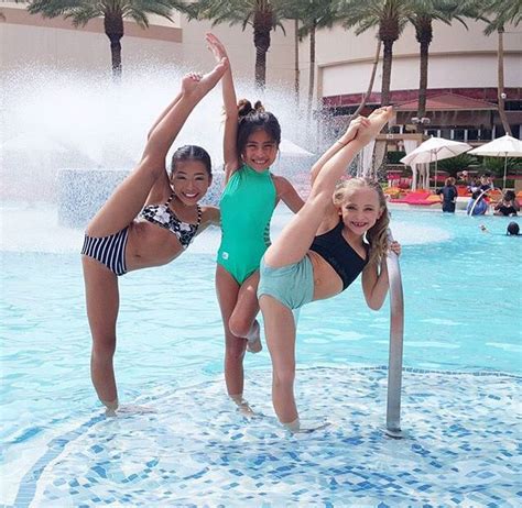 Three Girls In Swimsuits Are Standing On The Edge Of A Pool And Posing