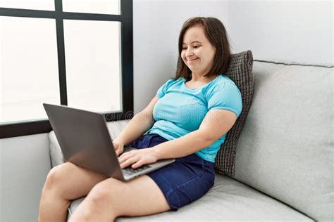 Brunette Woman With Down Syndrome Sitting On The Sofa Using Laptop At