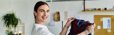 Un joven gay vistiendo una camisa blanca sonríe mientras sostiene una pieza de ropa en su