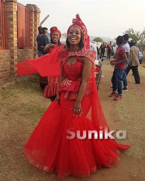 A Woman In A Red Dress Standing On The Side Of A Road With Other People