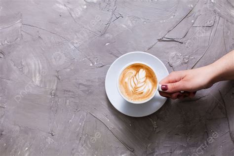 Female Hand Holding A Cup Of Cappuccino With Figure Cream Top View With