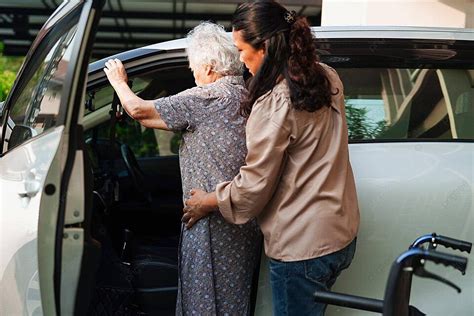 Assisting An Elderly Asian Woman With A Disability To Get Into Her Car