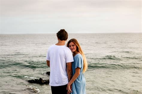 A Man And Woman Standing Next To Each Other Near The Ocean