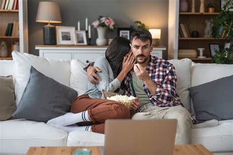 Couple Shocked Watching Horror Movie On Laptop Computer Sitting At Sofa